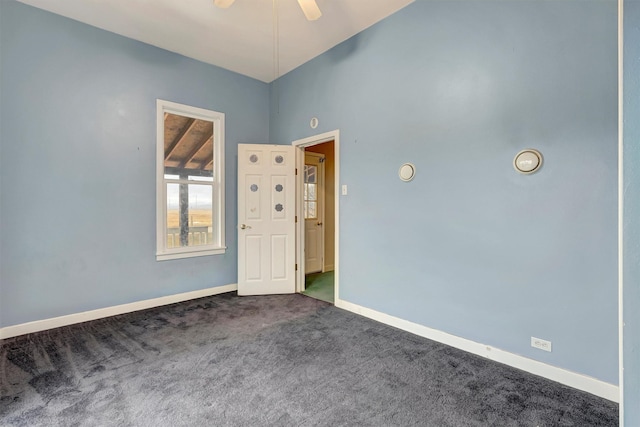 unfurnished room with a ceiling fan, dark carpet, and baseboards