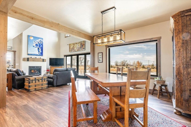 dining space with a lit fireplace, high vaulted ceiling, wood finished floors, and beam ceiling