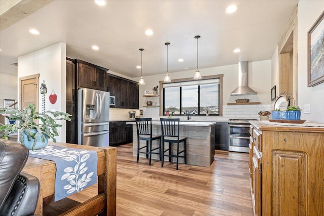 kitchen featuring wall chimney exhaust hood, appliances with stainless steel finishes, light countertops, a kitchen bar, and open shelves