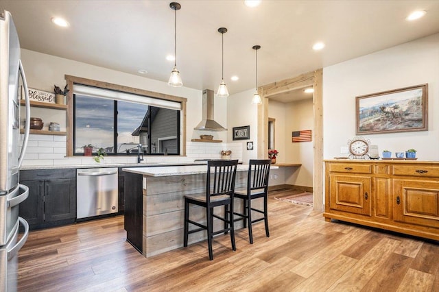 kitchen featuring appliances with stainless steel finishes, light countertops, light wood-style flooring, and wall chimney range hood