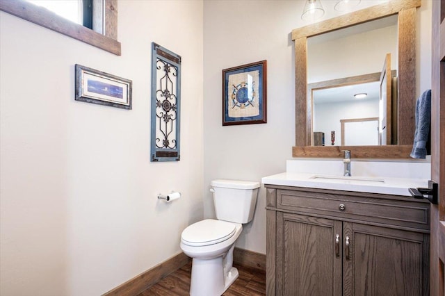 half bathroom featuring baseboards, vanity, toilet, and wood finished floors