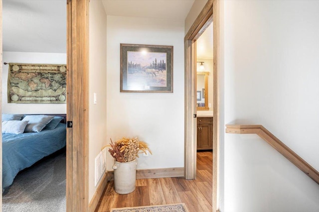 corridor with an upstairs landing, visible vents, light wood-style flooring, and baseboards