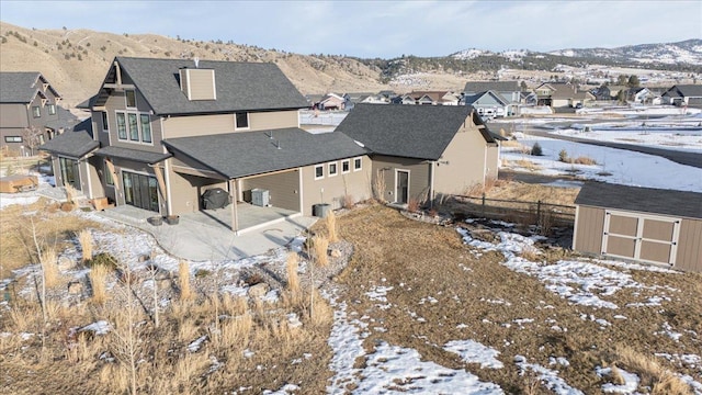 snow covered back of property featuring an outdoor structure, fence, a residential view, a shed, and a patio area