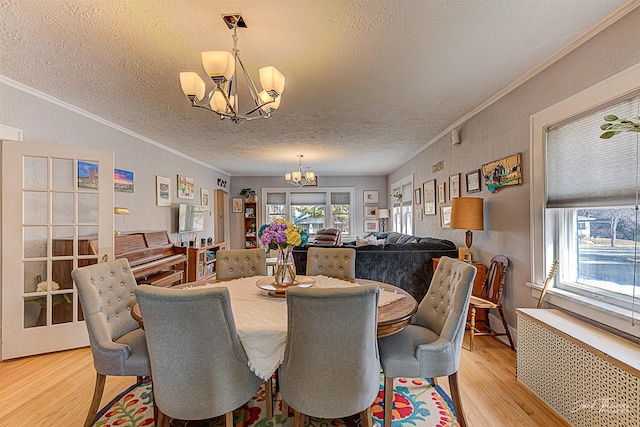 dining area featuring radiator, ornamental molding, an inviting chandelier, a textured ceiling, and light wood-style floors