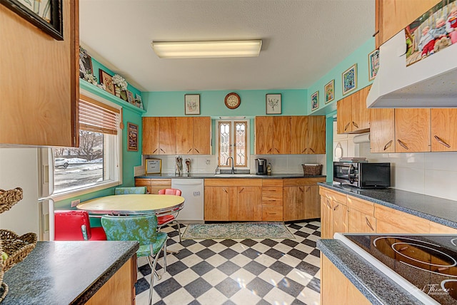 kitchen with dark countertops, freestanding refrigerator, a sink, dishwasher, and tile patterned floors