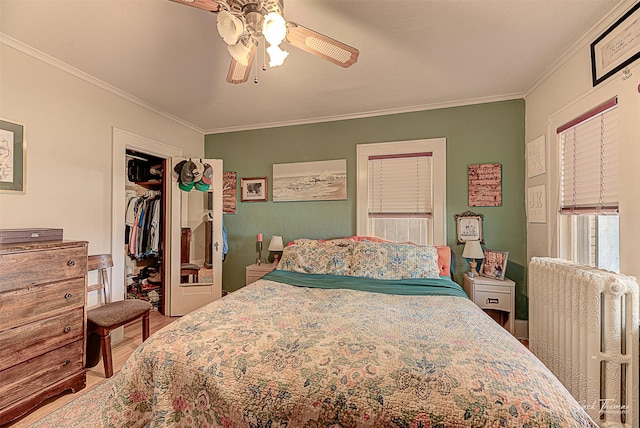 bedroom with a closet, a spacious closet, radiator heating unit, ornamental molding, and a ceiling fan