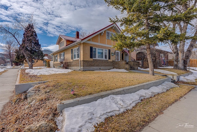 view of front facade with brick siding, a chimney, a front yard, and fence