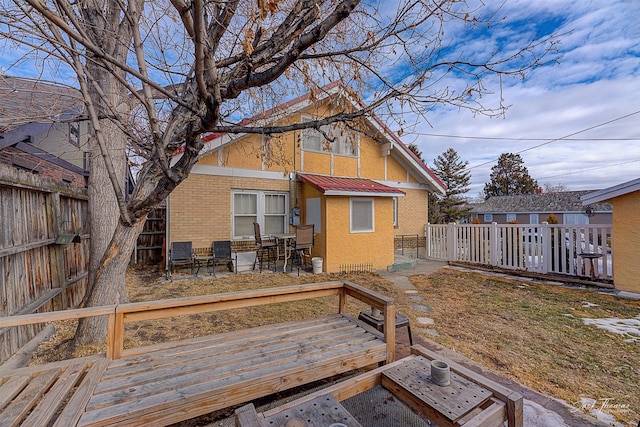 back of house with brick siding, stucco siding, metal roof, a fenced backyard, and a wooden deck