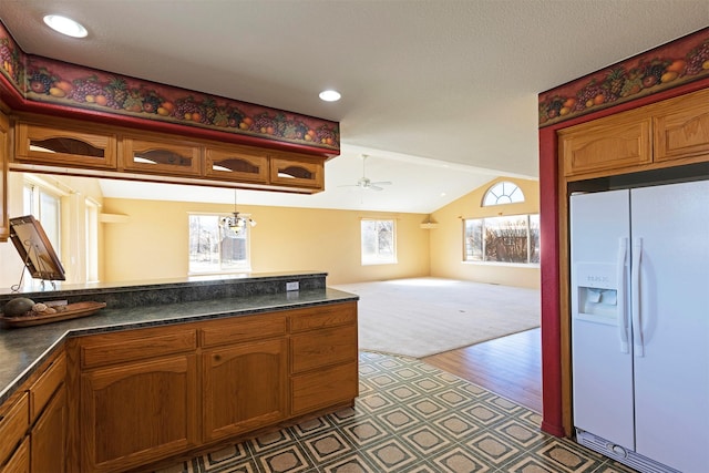 kitchen with white refrigerator with ice dispenser, dark countertops, brown cabinetry, a ceiling fan, and vaulted ceiling