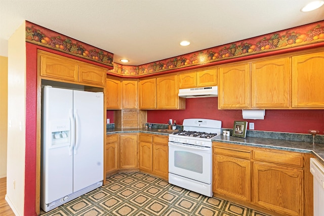 kitchen with dark countertops, white appliances, brown cabinets, and under cabinet range hood