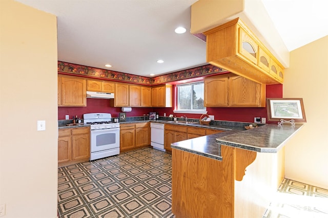 kitchen featuring a breakfast bar, dark countertops, a peninsula, white appliances, and under cabinet range hood