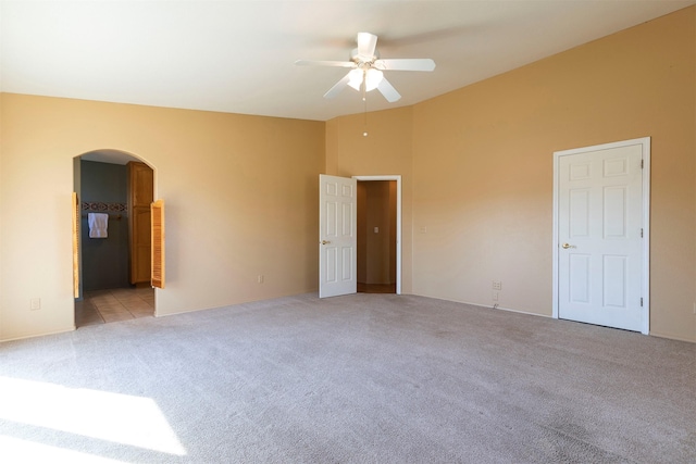 unfurnished bedroom with arched walkways, ceiling fan, connected bathroom, light colored carpet, and vaulted ceiling