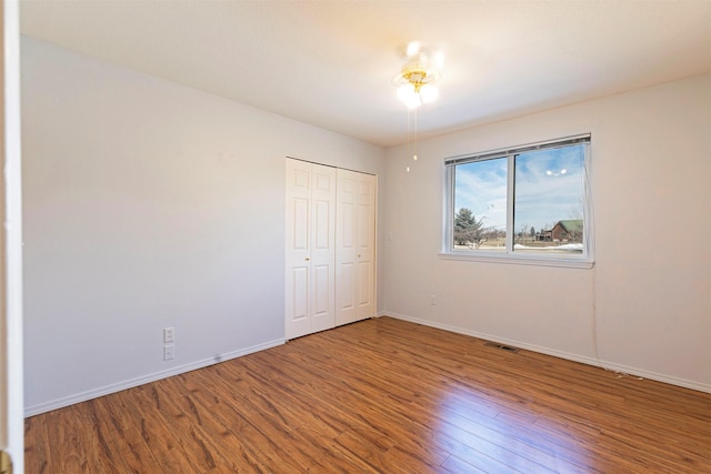 unfurnished bedroom featuring a closet, wood finished floors, visible vents, and baseboards