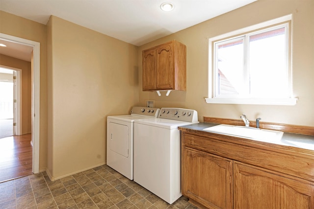 laundry area featuring cabinet space, baseboards, stone finish flooring, separate washer and dryer, and a sink