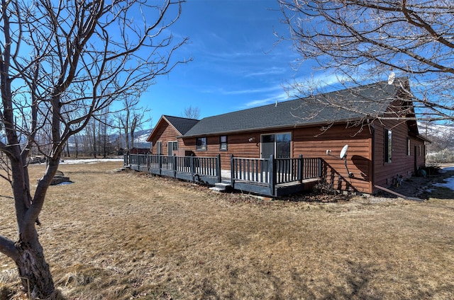 rear view of property with a deck, a lawn, and roof with shingles