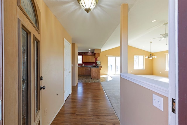 hall with lofted ceiling, dark wood-style floors, dark carpet, and an inviting chandelier