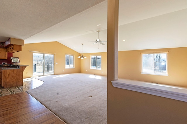 unfurnished living room featuring wood finished floors, vaulted ceiling, and ceiling fan with notable chandelier