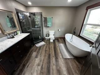 full bathroom featuring toilet, wood finished floors, vanity, a freestanding bath, and a shower stall