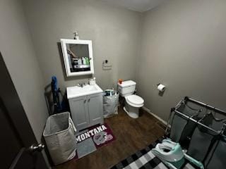 half bath with toilet, baseboards, wood finished floors, and vanity