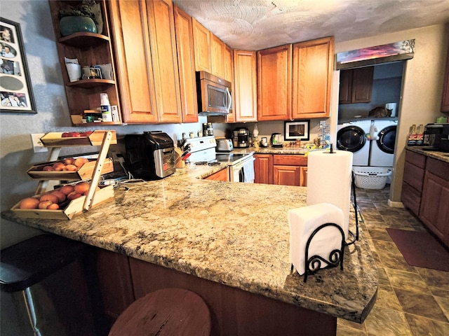 kitchen with light stone counters, washer and clothes dryer, stainless steel microwave, electric range, and stone finish floor