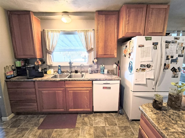 kitchen featuring brown cabinetry, white appliances, a sink, and stone finish flooring