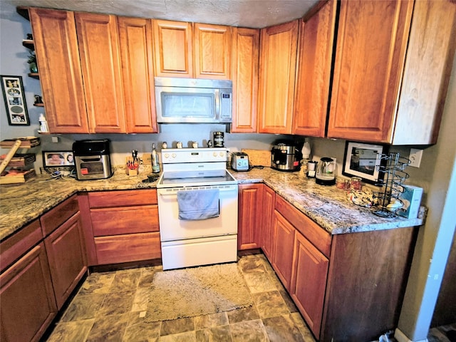 kitchen featuring light stone countertops, stainless steel microwave, brown cabinets, stone finish floor, and white electric range oven