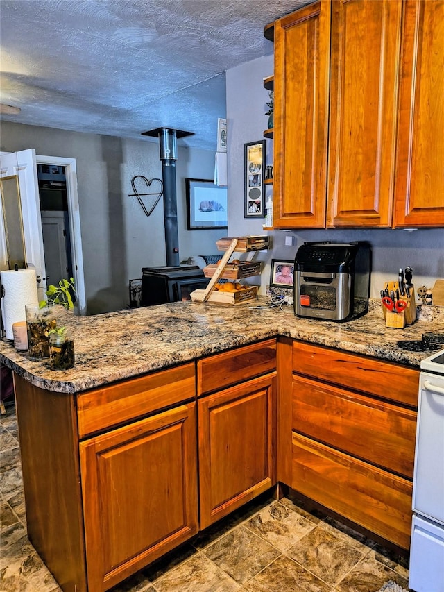 kitchen with a textured ceiling, a peninsula, white range with gas cooktop, brown cabinets, and a wood stove