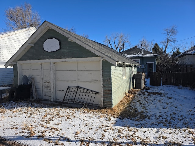 snow covered garage featuring a garage and fence