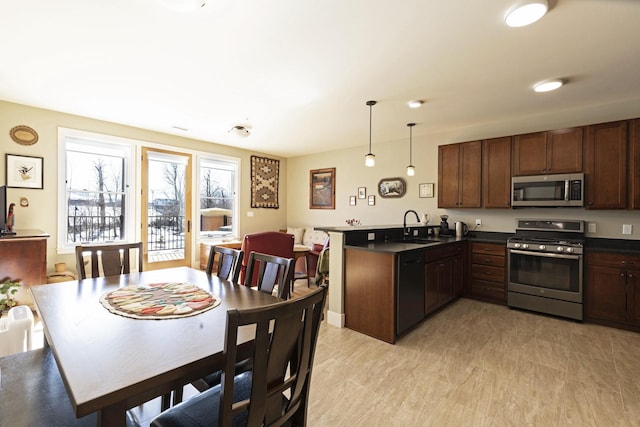 kitchen featuring dark countertops, a peninsula, stainless steel appliances, pendant lighting, and a sink