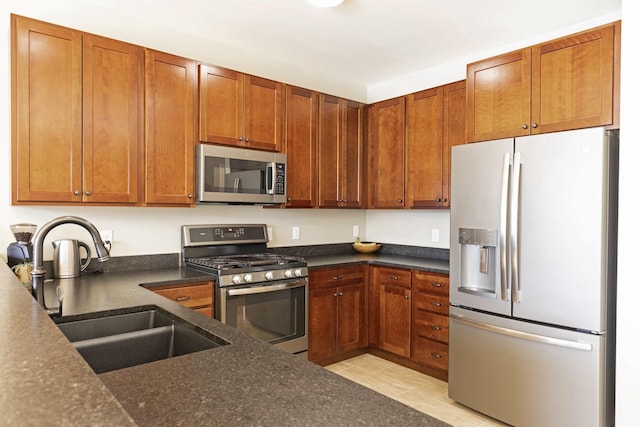 kitchen with dark stone countertops, appliances with stainless steel finishes, brown cabinetry, and a sink