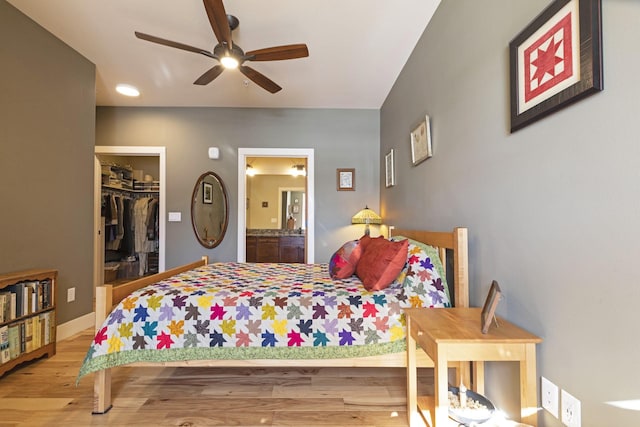 bedroom featuring a spacious closet, ensuite bathroom, a ceiling fan, wood finished floors, and baseboards