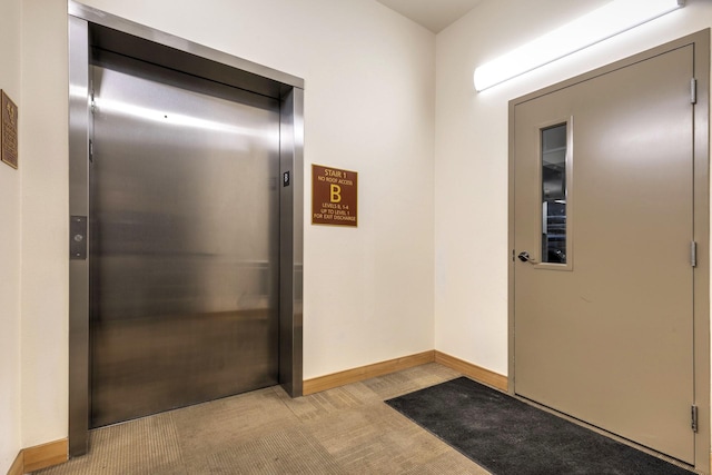 interior space featuring elevator, light colored carpet, and baseboards