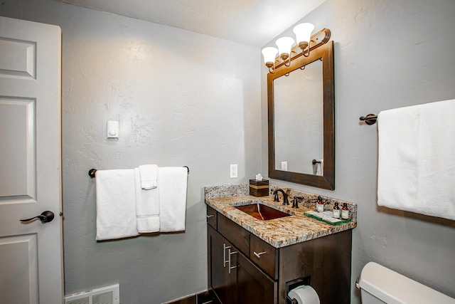 bathroom with toilet, a textured wall, vanity, and visible vents