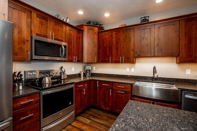 kitchen featuring dark stone counters, appliances with stainless steel finishes, dark wood-type flooring, a sink, and recessed lighting