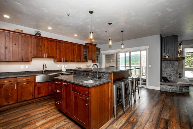 kitchen featuring an island with sink, dark wood-style flooring, a sink, and a kitchen breakfast bar