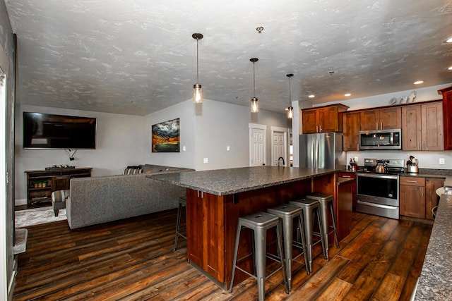 kitchen with dark countertops, appliances with stainless steel finishes, dark wood finished floors, and a center island