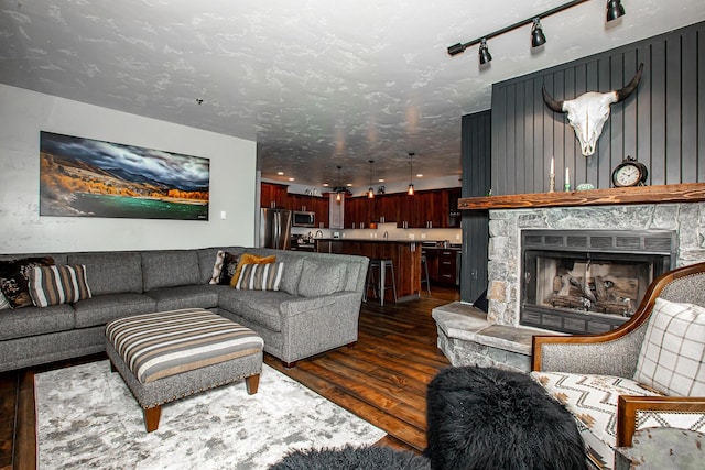 living room featuring dark wood-style flooring, a stone fireplace, and a textured ceiling