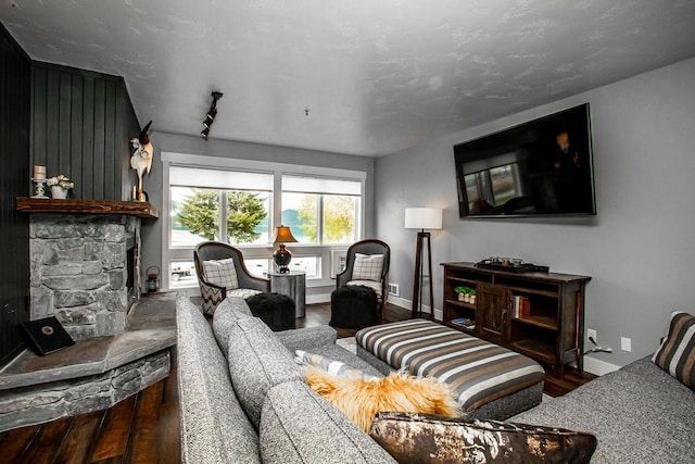 living area featuring a stone fireplace, baseboards, and wood finished floors