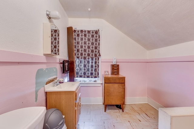 half bath with lofted ceiling, toilet, vanity, a textured ceiling, and baseboards