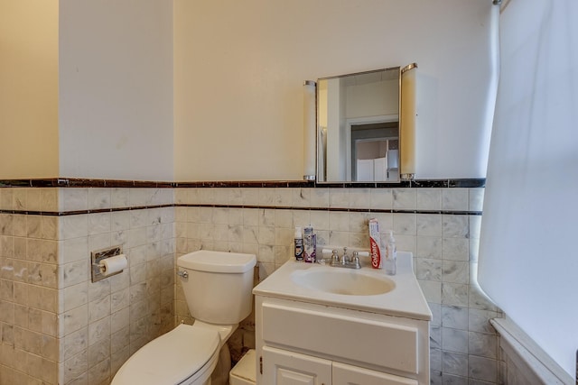 bathroom with tile walls, wainscoting, vanity, and toilet