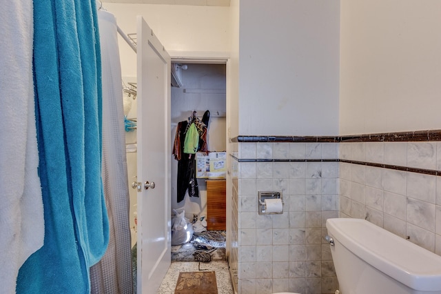 bathroom with toilet, a wainscoted wall, and tile walls