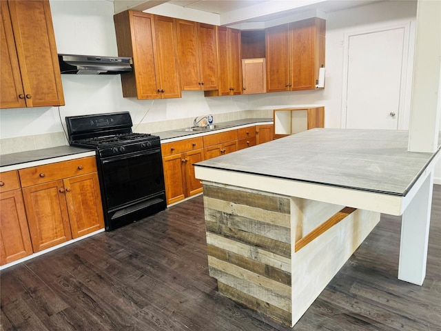 kitchen with dark wood finished floors, under cabinet range hood, a sink, brown cabinets, and black gas range