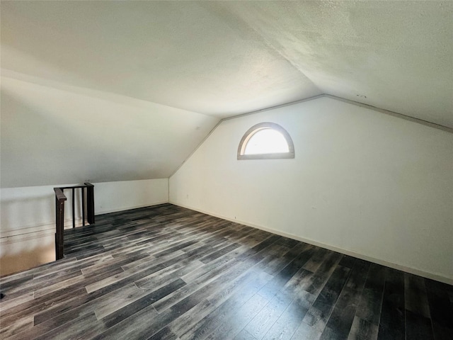 additional living space with dark wood-style flooring, vaulted ceiling, a textured ceiling, and baseboards