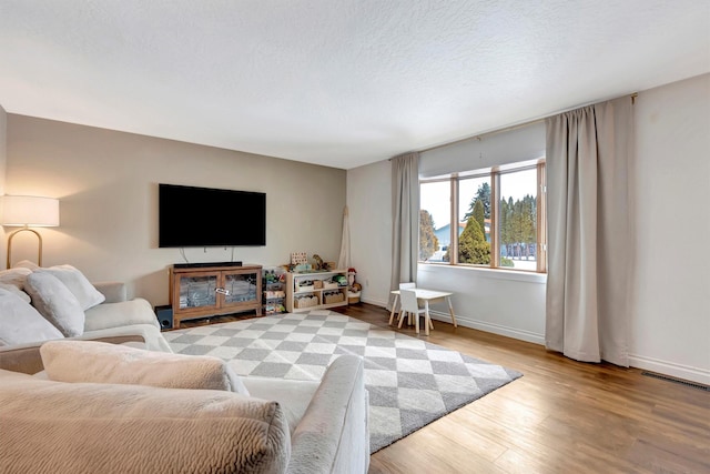 living area with visible vents, a textured ceiling, baseboards, and wood finished floors