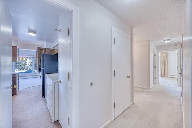 hallway featuring a textured ceiling, washer / dryer, and light colored carpet