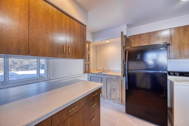 kitchen with washer / clothes dryer, light countertops, freestanding refrigerator, light carpet, and a sink