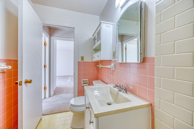 half bath with toilet, wainscoting, tile walls, and vanity