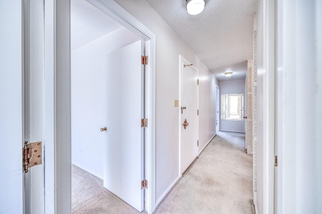 hallway with light colored carpet and a textured ceiling