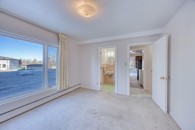 spare room featuring a baseboard radiator, a healthy amount of sunlight, light carpet, and baseboards