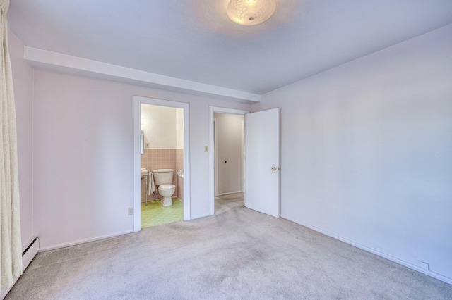 unfurnished bedroom featuring carpet, tile walls, baseboard heating, and ensuite bathroom